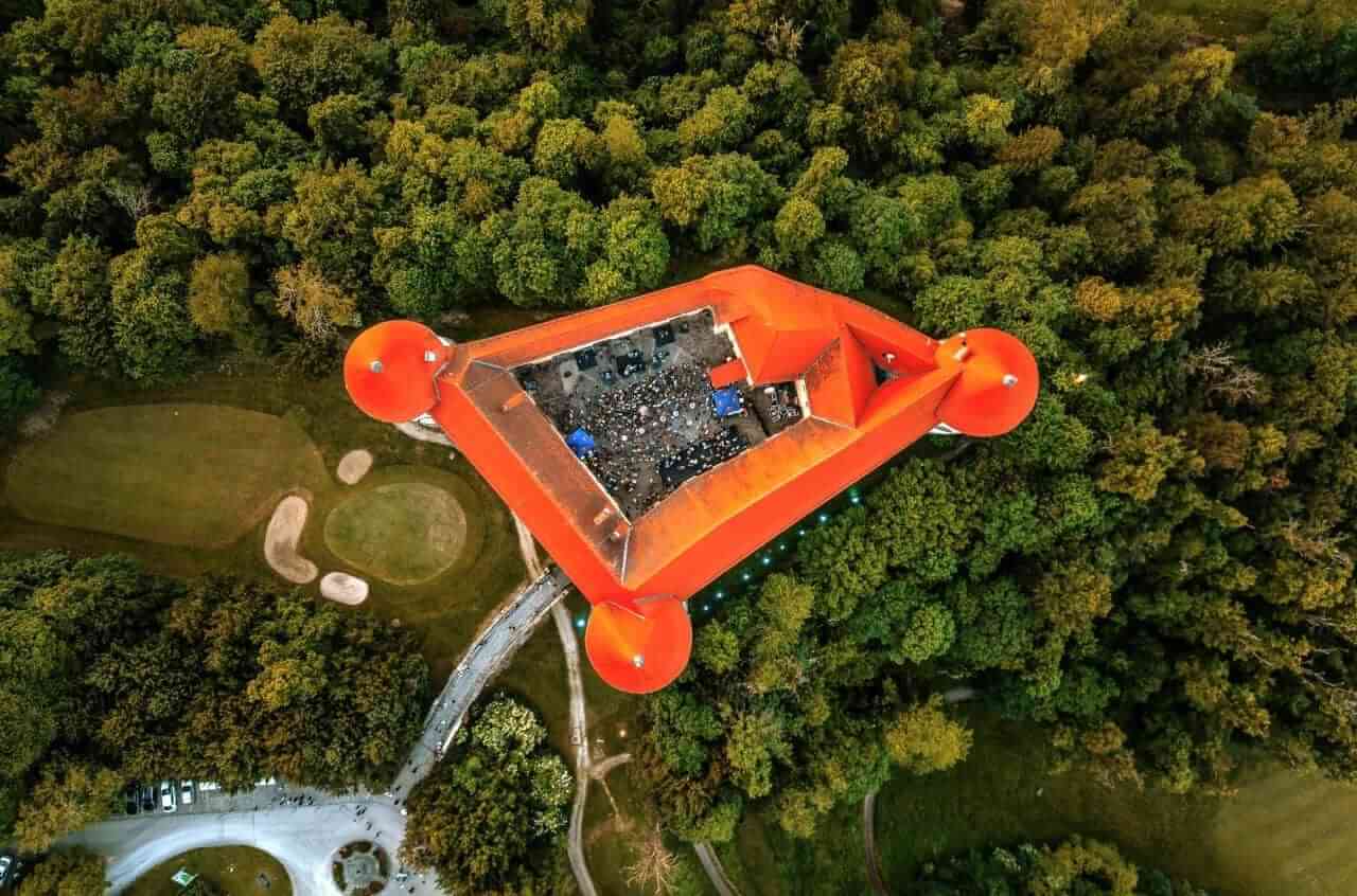 Mokrice Castle, Aerial view of an orange tower with four rounded pods at its corners standing among dense green trees.